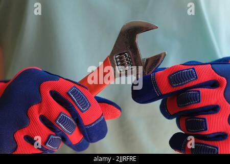 Person hands in protective work gloves holding spanner. Stock Photo
