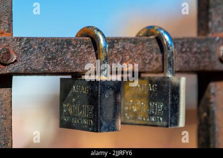 A closeup of two silver closed padlocks isolated on the rusty metal pole Stock Photo