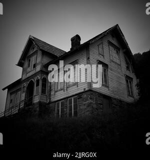 A low angle grayscale of an enormous abandoned ghost house with broken windows in Norway Stock Photo