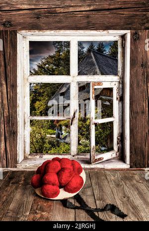 Original Black Forest Bollenhut lying on a wooden table in front of a wooden window with a view in the landscape Stock Photo
