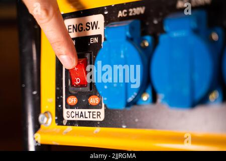 Red button for turning on and off a gasoline electric generator close-up. Finger presses the button Stock Photo