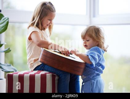 The best thing in the world is a big sister. two little sisters playing the guitar at home. Stock Photo