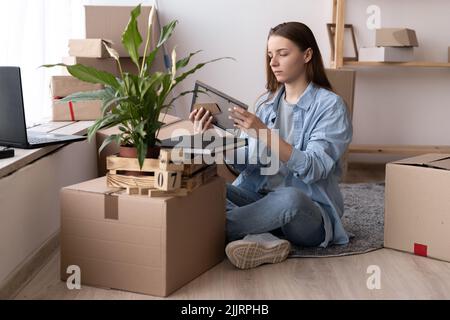 Young woman moving to new place sitting on floor hugging holding frame looking at photo cheerful Stock Photo