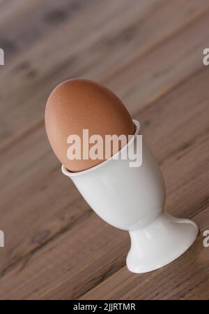 Breakfast egg in a white egg cup is on the wooden table, vertical format Stock Photo