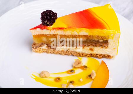 A closeup shot of a small blackberry on a Mango mousse cake slice on a white plate Stock Photo