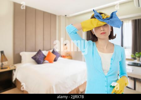 Exhausted Asian housewife wiping sweat from forehead and looking at camera while taking short break from spring clean in cozy bedroom, portrait shot Stock Photo