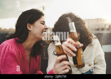 Two women having fun drinking beers outdoors laughing together - young people relaxing using alcohol - lifestyle concept Stock Photo