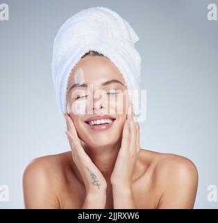 I CAN keep my hands to myself. Studio portrait of an attractive young woman moisturizing her face against a grey background. Stock Photo