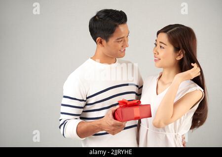 Celebrating Saint Valentines Day with Soulmate: handsome Asian man embracing his pretty young girlfriend while holding git box in hand, studio shot Stock Photo