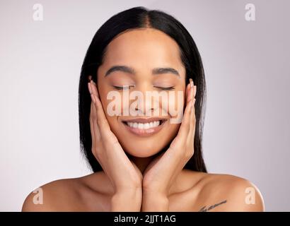 Keeping her hands to herself. an attractive young woman touching her face while posing against a pink background. Stock Photo