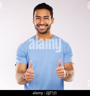 When youre positive, good things happen. Studio shot of a young man showing a thumbs up gesture against a white background. Stock Photo