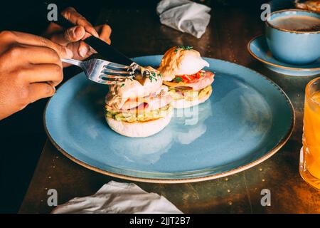 A faceles person cutting the Eggs Benedict on the breakfast plate Stock Photo
