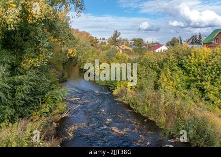Autumn landscape. River within the city of Sterlitamak, Republic of Bashkortostan. Golden foliage grow on shore, under blue sky with clouds Stock Photo
