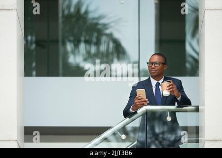 Pensive young business executive with coffee and smartphone Stock Photo