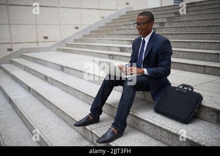 Smiling young businessman sitting on steps and working on laptop Stock Photo