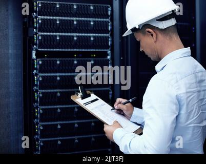 Wifi running well Check. a young man making notes while working in a server room. Stock Photo