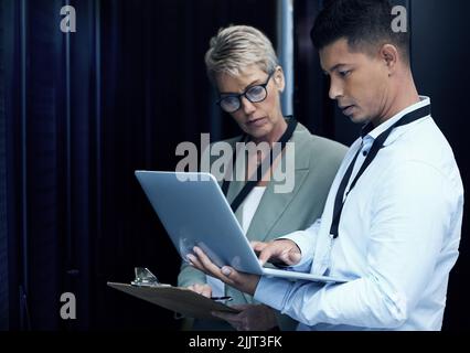 Teaming up to take on any IT infrastructure. two technicians working together in a server room. Stock Photo
