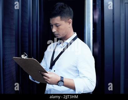 In the world of tech, he knows whats up. a young man making notes while working in a server room. Stock Photo