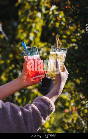 A vertical shot of two young people holding refreshing colorful drinks outside Stock Photo
