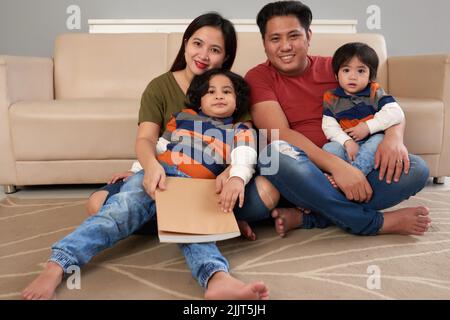 Happy mother, father and their two sons sitting on the floor Stock Photo