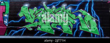 A panoramic shot of green letters of social graffiti street art with thunder behind it on black wall Stock Photo
