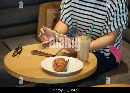 Cropped image of female student eating lunch and writing down ideas for essay Stock Photo