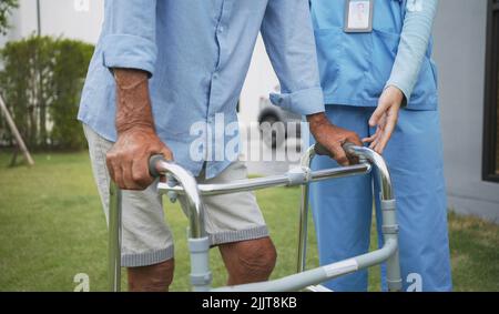 Senior elderly man patient doing physical therapy with caregiver. Attractive specialist carer women help and support older mature male practice walkin Stock Photo