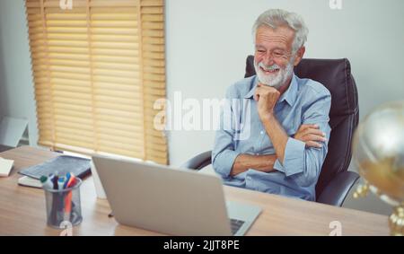 Happy senior older man using laptop computer at work desk. Stock Photo