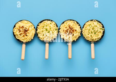 German spaetzle in small pans aligned on a blue table view from above. German noodles with cheese, topped with chives and roasted onion. Stock Photo