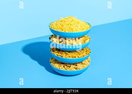 Plates with raw pasta stacked on a blue table in bright light. Various types of uncooked pasta in blue plates on a colorful background. Stock Photo