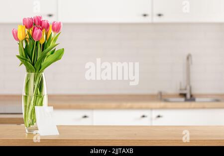 Bouquet of beautiful tulips on kitchen table with blank sheet of paper Stock Photo