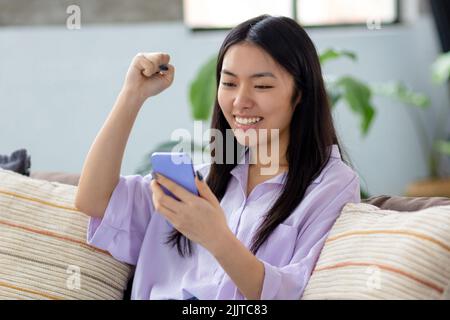 Excited young Asian woman using mobile phone shopping online sitting Big sales  Stock Photo