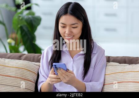 Young woman using mobile phone chatting online Smiling female looks at the smartphone shopping online Stock Photo