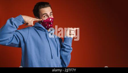 Young excited man wearing face mask pointing fingers aside isolated over red background Stock Photo