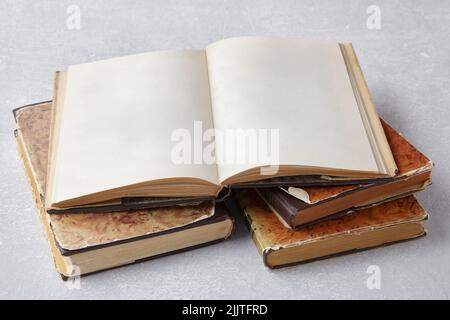 Open vintage book or notebook in a super jacket on a stack of old shabby books on a pale gray concrete table Stock Photo