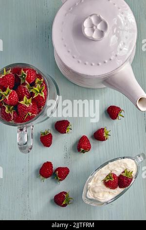 Red raspberries in a glass bowl with cream and in a cup are sprinkled on a blue wooden table Stock Photo