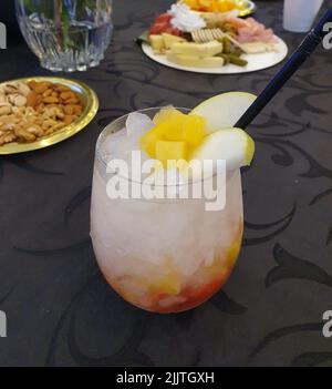 A closeup of refreshing cocktail with apple slices and ice cubes on the table Stock Photo