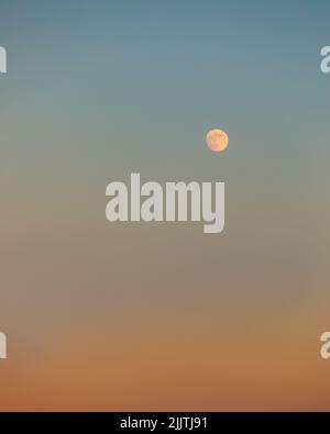 A moon appearing in sky during sunset Stock Photo