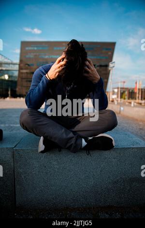 A man sitting alone in the street and looking upset or with a pain in the head Stock Photo