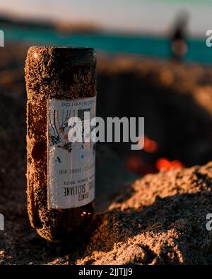 A glass bottle turned upside down in the sands on bokeh background Stock Photo
