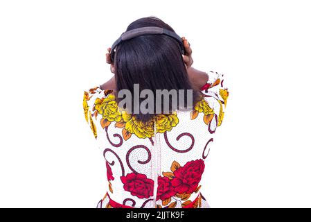 a woman in a corsage standing on a white background listening to music using headphones while giving her back to the camera Stock Photo