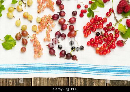 Summer ripe berries (red, pink and black currants, gooseberries, raspberry, wild strawberries) on vintage linen towel. Stock Photo