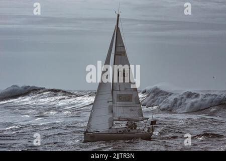 Porto, Portugal - December 31, 2015: Intrepid sailing boat entering in the mouth of the Douro river harbor, seeing dangerous stormy waves at the rear Stock Photo