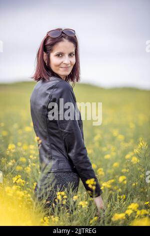 A vertical shot of a young Caucasian female in the field of yellow flowers Stock Photo