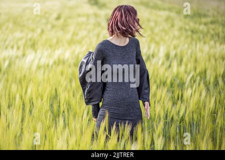 A beautiful portrait of a young Caucasian woman standing among long green grass in the field on a sunny day Stock Photo