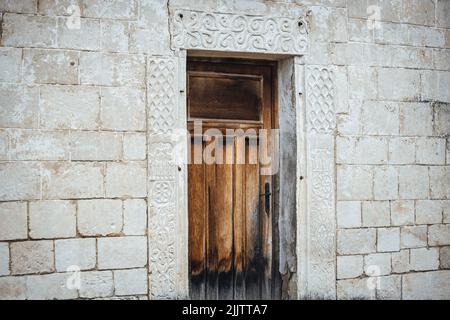 An old wooden door surrounded by white bricks of a building Stock Photo