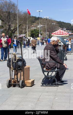 A vertical shot of an old man sitting on a bench while working and talking by phone in Istanbul, Turkey Stock Photo