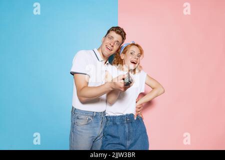 Portrait of young couple with funny expression turning on TV isolated over pink blue studio background. Movie time Stock Photo