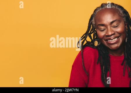 Black woman with dreadlocks smiling happily while standing against a studio background. Cheerful black woman embracing her natural hair with confidenc Stock Photo