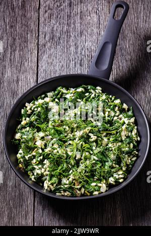 Spanakorizo, Greek spinach and rice pilaf with lemon, dill, spring onion in skillet on dark wooden table, vertical view from above Stock Photo